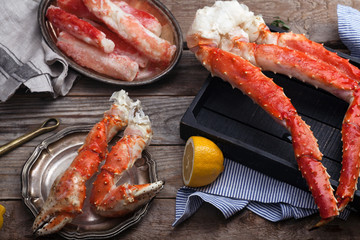 Fresh crab claws and different types of crab meat on black wooden tray on vintage wooden background with vintage plates and lemon slices. Horizontal composition