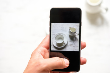 A man takes a picture of an empty cup of coffee on a smartphone