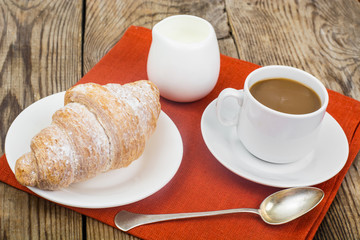 Breakfast. Fresh croissant and cup of coffee with milk on wooden
