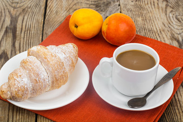 Breakfast. Fresh croissant and cup of coffee with milk on wooden