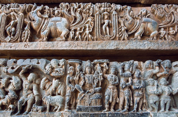 Ornate bas relief with historical Indian background, Lord Vishnu sitting, Krishna and humans in stone. 12th century Hoysaleshwara temple in Halebidu, India