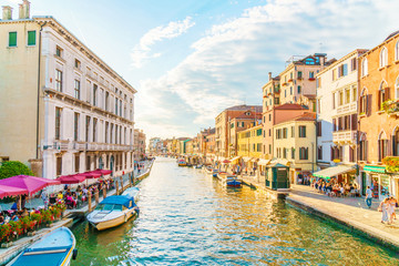 Bright Venice street with canal and boats and typical Venetian buildings.