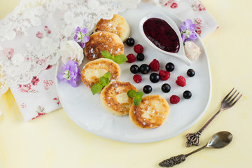 Cottage cheese pancakes on a plate with berries on yellow background