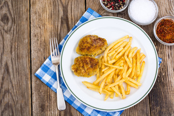 White plate with French fries and meat cutlets on wooden table