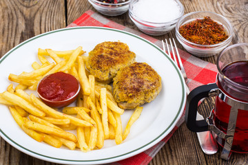White plate with French fries and meat cutlets on wooden table
