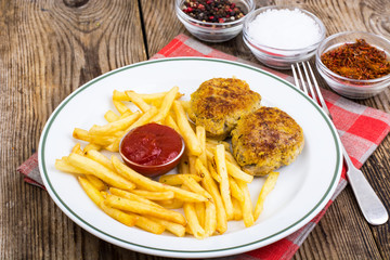 White plate with French fries and meat cutlets on wooden table