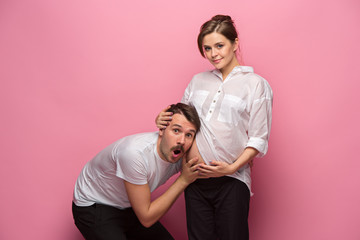 Obraz premium Handsome man is listening to his beautiful pregnant wife's tummy and smiling