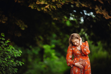 Fototapeta na wymiar Beautiful pregnant woman in orange dress poses in the forest