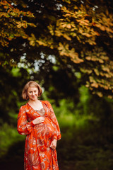 Beautiful pregnant woman in orange dress poses in the forest