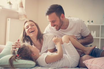 Parents having fun with their little daughter on bed. Family spending time at the morning.