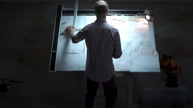 Young engineer standing at the white board with drawing and plan back view. Male architect standing at drawing board and floor plan with pencil in hand at office