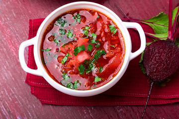 Ukrainian traditional borsch. Russian vegetarian red soup  in white bowl on red wooden background. Top view.  Borscht, borshch with beet.