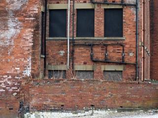 derelict abandoned commercial or factory type building with boarded up windows decaying bricks and...