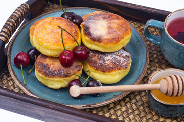 Delicious curd cheese cakes with honey and cherries on tray