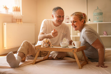 Senior couple having healthy breakfast together in bed.