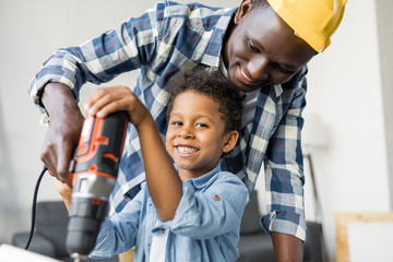 adorable african-american father and son using drill
