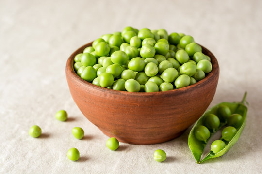 Fresh green peas in ceramic bowl on gray stone background