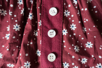 Three white buttons on maroon linen with floral print