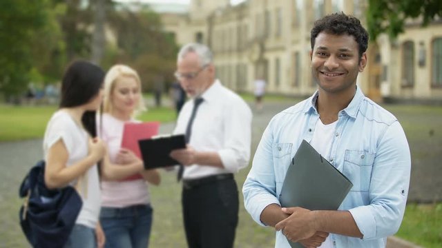 Happy Hispanic student standing near college and looking into camera, education