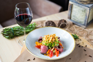 Close-up of salad with beef, cherry tomatoes, pepper, lettuce, background of a glass of red wine, rosemary, beautiful trendy serve, restaurant, dinner, lunch, delicious food, high-cuisine