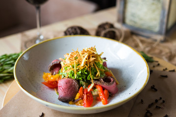 Close-up of salad with beef, cherry tomatoes, pepper, lettuce, background of a glass of red wine, rosemary, beautiful trendy serve, restaurant, dinner, lunch, delicious food, high-cuisine