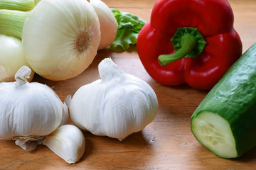 Fresh vegetables on a wooden surface. Ingredients for preparation of salad: garlic, onions, cucumber, sweet pepper and lettuce.