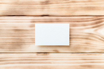 Closeup mockup of white blank horizontal business card at light natural wooden background.