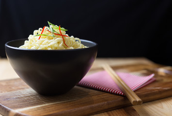 Instant noodles in black bowl on wood background, Asian meal on a table
