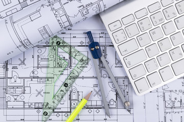 Architectural blueprints drawings of the modern house with computer keyboard. Architectural blueprints and blueprint rolls and a drawing instruments on the worktable. Drawing compass, plans.