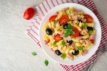 Fusilli pasta salad with tuna, tomatoes, black olives and basil on gray stone background