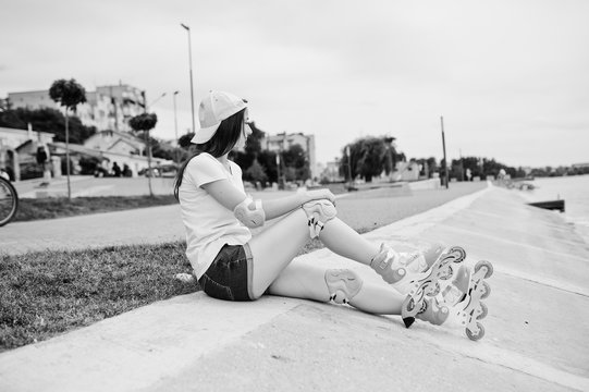 Portrait of a gorgeous young woman in casual clothes and cap sitting on the ground next to the lake. Black and white photo.