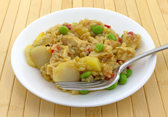 Rice with chicken and vegetables meal on a plate with a fork atop a wood place mat.