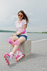 Portrait of an attractive young woman in shorts, t-shirt, sunglasses and rollerblades sitting on...