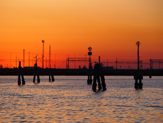 Fototapeta premium sunset on the lagoon in venice with orange sky reflected in the water and bridge in the background