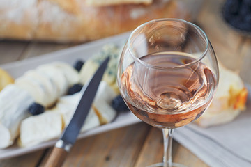 A glass of rose wine served with cheese plate, blackberries and baguette
