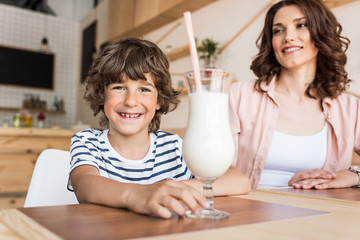 happy boy with glass of milkshake and his smiling mother blurred on background