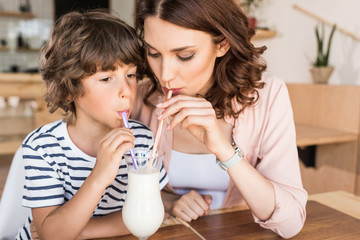 Obraz na płótnie Canvas mother and son drinking milkshake together in cafe
