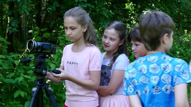 Children with video camera on tripod make movies about nature of green park. Babies outdoors in summer are creative work of cinema. Beautiful footage. Interesting to look at world in childhood.