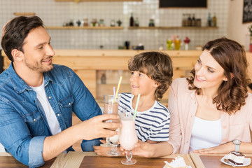 happy young family drinking milkshakes in cafe and spending time together