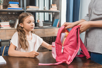 mother and pensive little daughter preparing backpack for school