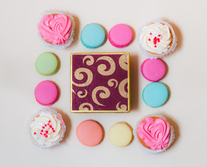 Fototapeta na wymiar Macaroons, cupcakes and gift box on beige background. Top view
