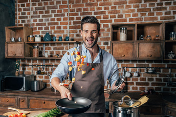 handsome young man with apron frying vegetables for pasta