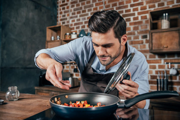 handsome young man with apron frying vegetables