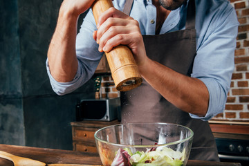 cropped shot of man adding pepper with mill into salad