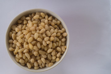 Small ceramic bowl full of pine nuts on the grey background