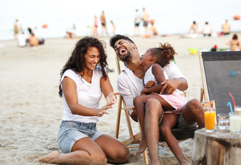 Young mixed race family sitting and relaxing  at the beach on beautiful summer day.Daughter lies in...