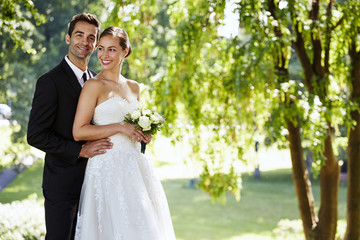 Newly wedded happy couple smiling in sunlit park