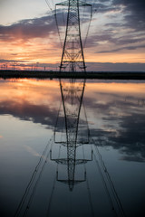 Electricity pylon reflected in lake water at sunset