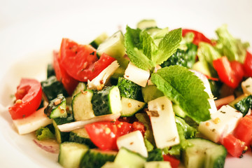 Salad of cucumbers, tomatoes, mozzarella cheese, lettuce, onions, spices and olive oil. Healthy food. Tomato, cucumber, mozzarella cheese, onion, lettuce.