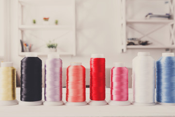 Colorful thread spools on wooden table close up